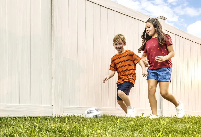 brother and sister playing soccer next to vinyl privacy fence